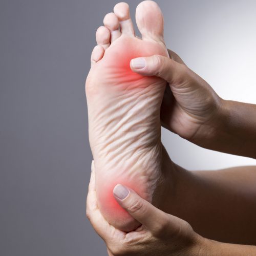 Pain in the foot. Massage of female feet. Pain in the human body on a gray background with red dot