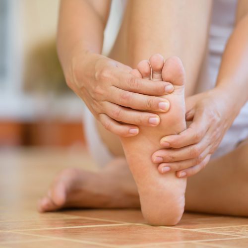 Closeup young woman feeling pain in her foot at home. Healthcare and medical concept.